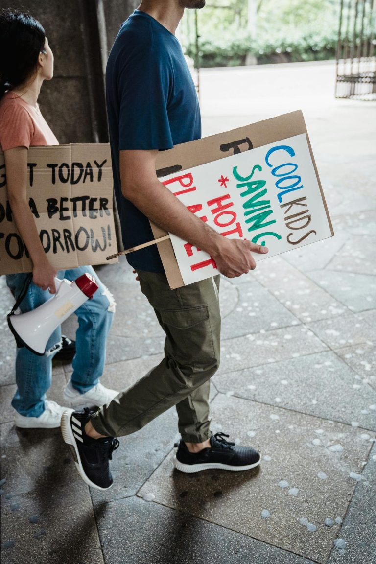 Two people holding protest signs and a megaphone walking on a city street.